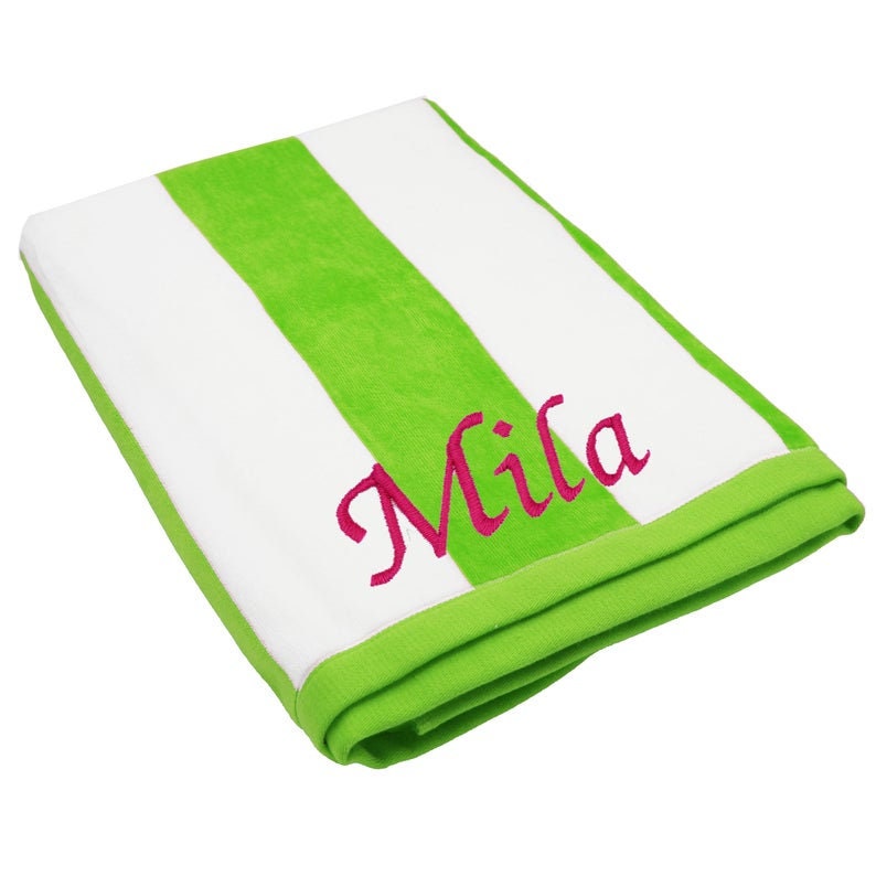 May include: A folded beach towel with a green and white striped pattern. The towel has the name "Mila" embroidered in pink script. The edges are trimmed with a solid green border.