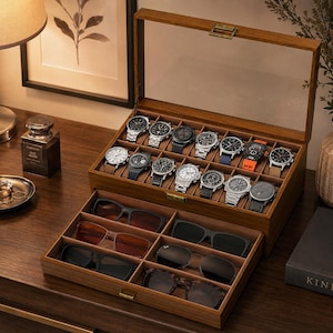 May include: A wooden watch and eyewear storage box featuring a clear glass lid, a top compartment with twelve individual watch slots, and a pull-out bottom drawer with six sections for sunglasses, all lined with a soft brown interior fabric.