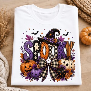 Può includere: Una t-shirt bianca con la scritta SPOOKY in grandi lettere colorate e decorate. Il design include un cappello da strega, zucche, un grande fiocco a quadri, fantasmi, pipistrelli e foglie autunnali nei toni dell'arancione, viola e nero.