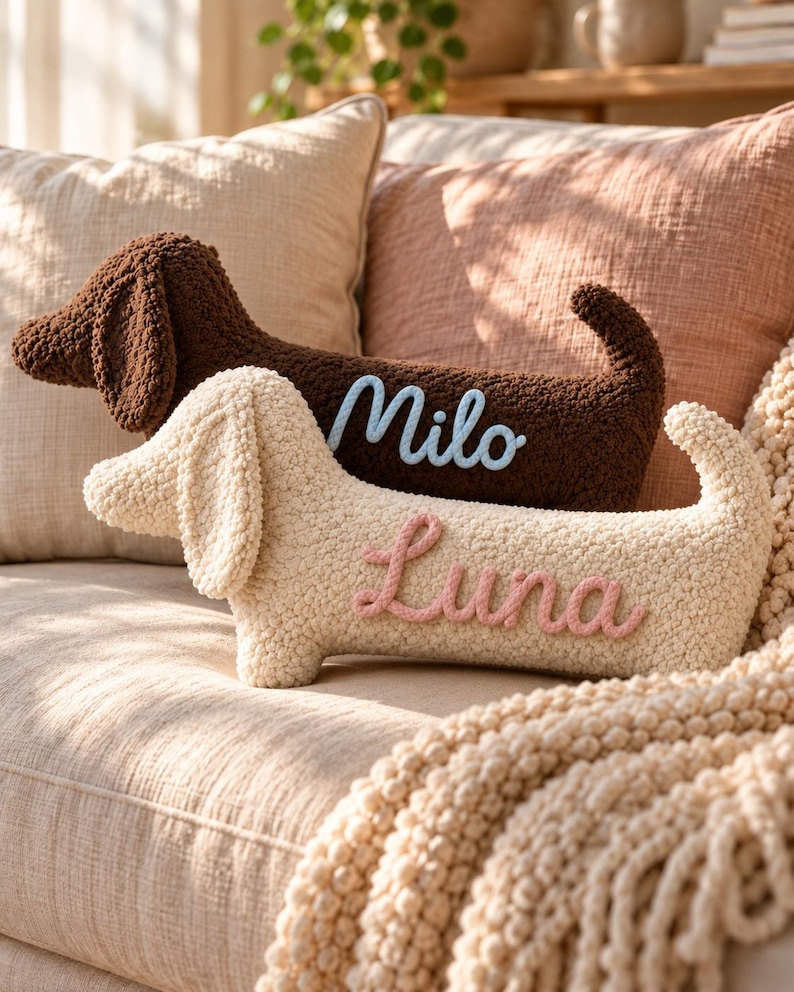 May include: Two dachshund-shaped throw pillows made of textured, curly fabric. The dark brown pillow features the name Milo in light blue script, while the cream-colored pillow features the name Luna in pink script, both stitched onto the side.