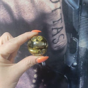 May include: A spherical clear resin paperweight containing multiple metallic brass-colored bullet casings of varying sizes arranged inside the transparent orb, showcasing the cylindrical shapes and primer ends of the ammunition components.