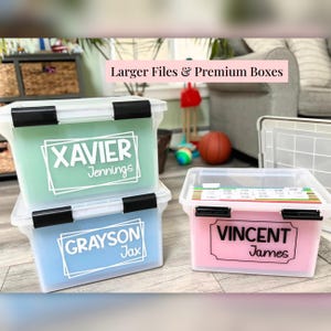 May include: Three clear plastic storage bins with black locking lids. The top bin contains a light green insert labeled XAVIER Jennings. The bottom bin has a light blue insert labeled GRAYSON Jax. The right bin holds pink files labeled VINCENT James.