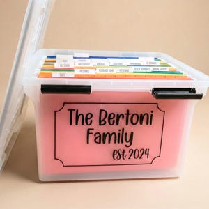 May include: A clear plastic file storage box with a black latch and a pink label on the front that reads The Bertoni Family est 2024. Inside are colorful hanging file folders with white tabs labeled for taxes, passports, and insurance.