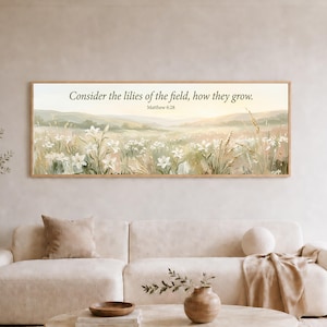 May include: A rectangular wall art print in a wooden frame featuring a landscape painting of a field of white lilies. The text "Consider the lilies of the field, how they grow. Matthew 6:28" is printed in dark lettering across the upper center.