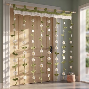 Puede incluir: Una cortina de puerta tejida a ganchillo con un faldón festoneado en blanco y verde y tiras verticales colgantes. Cada tira está decorada con pequeñas flores blancas tejidas y hojas verdes, suspendida de una barra de madera.