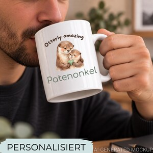 Könnte beinhalten: Eine weiße Keramiktasse mit einer braunen Illustration von zwei Ottern, die ein kleines grünes Herz halten. Der Text über den Ottern lautet "Otterly amazing" in Braun, und der Text darunter lautet "Patenonkel" in einem gedeckten Grünton.
