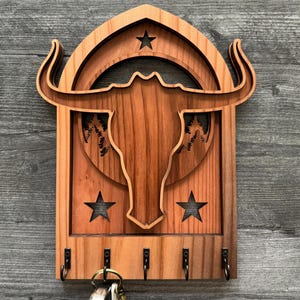 May include: Wooden key holder with a carved bull's head design, a crescent moon, and stars. The key holder has five hooks for hanging keys.