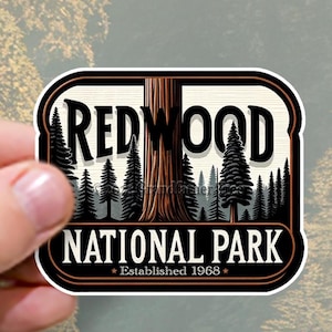 Pode incluir: Um adesivo de estilo vintage com um design marrom e branco. Apresenta uma grande árvore de sequoia com o texto "Redwood National Park" e "Estabelecido em 1968" em uma faixa preta.
