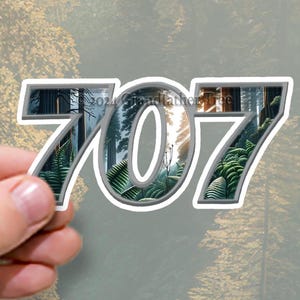 Op de afbeelding: Een grijze en witte sticker met het nummer 707. De nummers zijn wit omrand en hebben een bos scène binnenin.