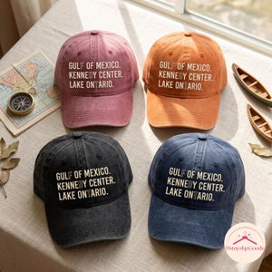 以下が含まれることがあります： ピンク、オレンジ、ブラック、ブルーの4つの野球帽。それぞれに「GULF OF MEXICO. KENNEDY CENTER. LAKE ONTARIO.」という白い文字がプリントされています。キャップはヴィンテージ風の仕上げで、構造化されたクラウン、カーブしたつば、上部にボタンが付いています。