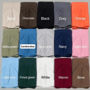 May include: A hoodie color chart featuring fifteen folded hoodies in various colors including sand, chocolate, black, grey, orange, military green, Carolina blue, sport grey, navy, light pink, light blue, forest green, white, maroon, and brown.
