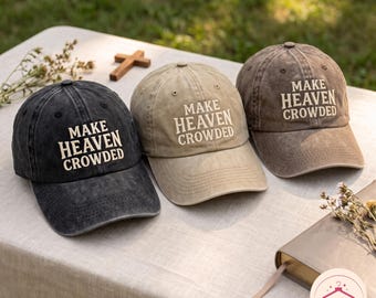 May include: Three baseball caps in charcoal, tan, and brown, each featuring a distressed fabric finish and the embroidered text MAKE HEAVEN CROWDED in a light-colored font. The caps have a curved brim and a structured crown with eyelet details.