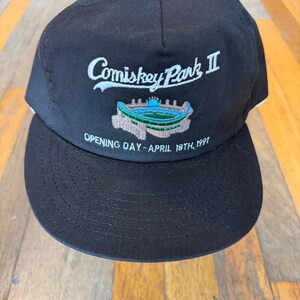 May include: A black baseball cap featuring white embroidered text that reads Comiskey Park II, a colorful embroidered graphic of a stadium, and the text OPENING DAY - APRIL 18TH, 1991 stitched in white thread on the front panel.