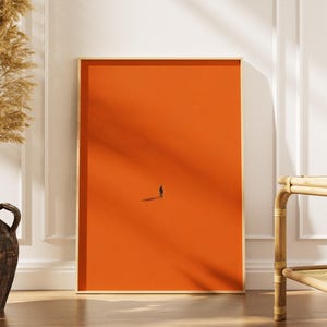 Peut inclure: Une impression d'art mural rectangulaire présentant un fond orange vif et uni avec une seule petite silhouette sombre d'une personne debout au centre inférieur, projetant une ombre longue et fine sur la surface orange plate et monochrome.