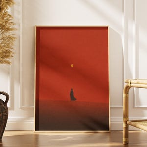 Könnte beinhalten: Ein rechteckiges gerahmtes Wandbild mit einer minimalistischen Landschaft, bestehend aus einem tiefroten Himmel, einer kleinen gelben Sonne und der dunklen Silhouette einer einsamen Figur auf einem dunkelbraunen Horizont, in einem hellen Holzrahmen.