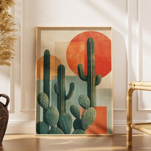 Op de afbeelding: Een rechthoekige wandkunstprint met een woestijnscène met groene saguaro- en vijgcactussen tegen een achtergrond van overlappende geometrische vormen in crème, lichtblauw en grote cirkels in levendig oranje en rood.