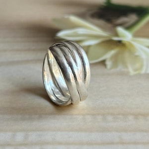 May include: A silver ring featuring a multi-band design with several interconnected, smooth, polished metal strands that wrap around the finger. The ring has a reflective, metallic finish and a rounded, continuous structure with no visible gaps.