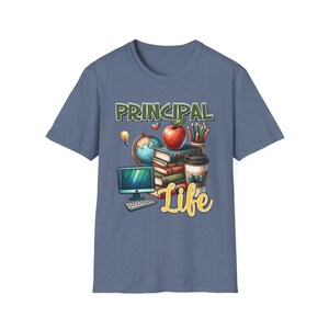May include: A slate blue t-shirt featuring a graphic print with the text PRINCIPAL Life. The design includes a computer monitor, a globe, a red apple, a stack of books, a cup of coffee with a blue bow, and a container of coloured pencils.