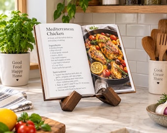 Può includere: Un leggio in legno che sostiene un libro aperto intitolato Mediterranean Chicken, con una ricetta completa di ingredienti e istruzioni accanto a una foto di pollo, pomodorini, olive e fette di limone su un piano di lavoro in marmo.