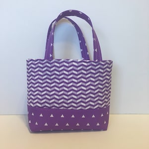 Puede incluir: Bolso de mano morado con un patrón de chevron blanco y un fondo morado con acentos de triángulos blancos.