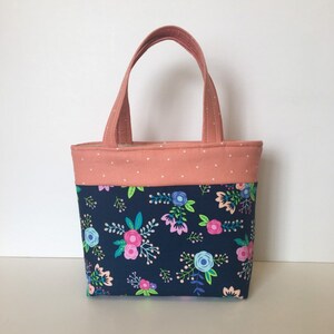 May include: A small tote bag with a navy blue floral print and a coral pink top with white polka dots. The bag has two coral pink handles.