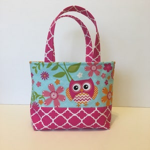 May include: A small pink and blue tote bag with a pink owl and floral print. The bag has two pink handles with a white and pink geometric pattern.
