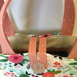May include: A pink tote bag with white polka dots and floral print. The bag has a white fabric lining and a pink button closure.
