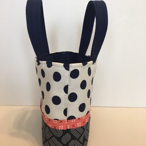 May include: A small tote bag with navy blue handles and a white fabric with black polka dots. The bottom of the bag is made of a black fabric with white polka dots and a pink and white stripe.