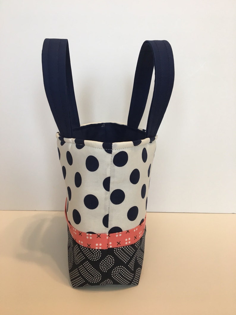 May include: A small tote bag with navy blue handles and a white fabric with black polka dots. The bottom of the bag is made of a black fabric with white polka dots and a pink and white stripe.