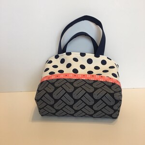 May include: A small, navy blue and white polka dot tote bag with a pink and white ribbon and a navy blue and white heart pattern on the bottom.