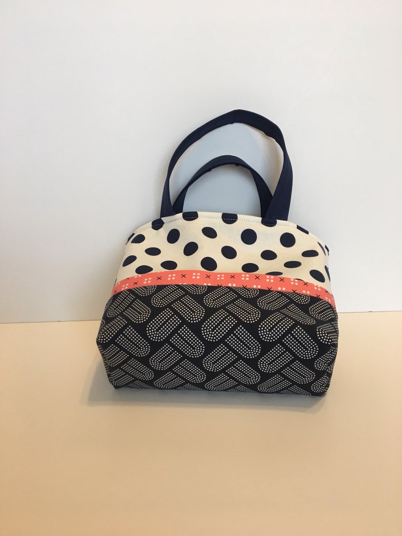 May include: A small, navy blue and white polka dot tote bag with a pink and white ribbon and a navy blue and white heart pattern on the bottom.