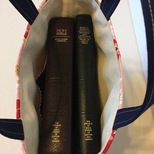 May include: A floral print tote bag with navy blue handles holds two books. One is a brown Holy Bible, King James Version. The other is a dark green Book of Mormon, Doctrine and Covenants, Pearl of Great Price. The bag's interior is a light beige.