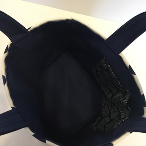 May include: A white and navy blue tote bag with a black mesh pocket inside. The bag has two navy blue handles.