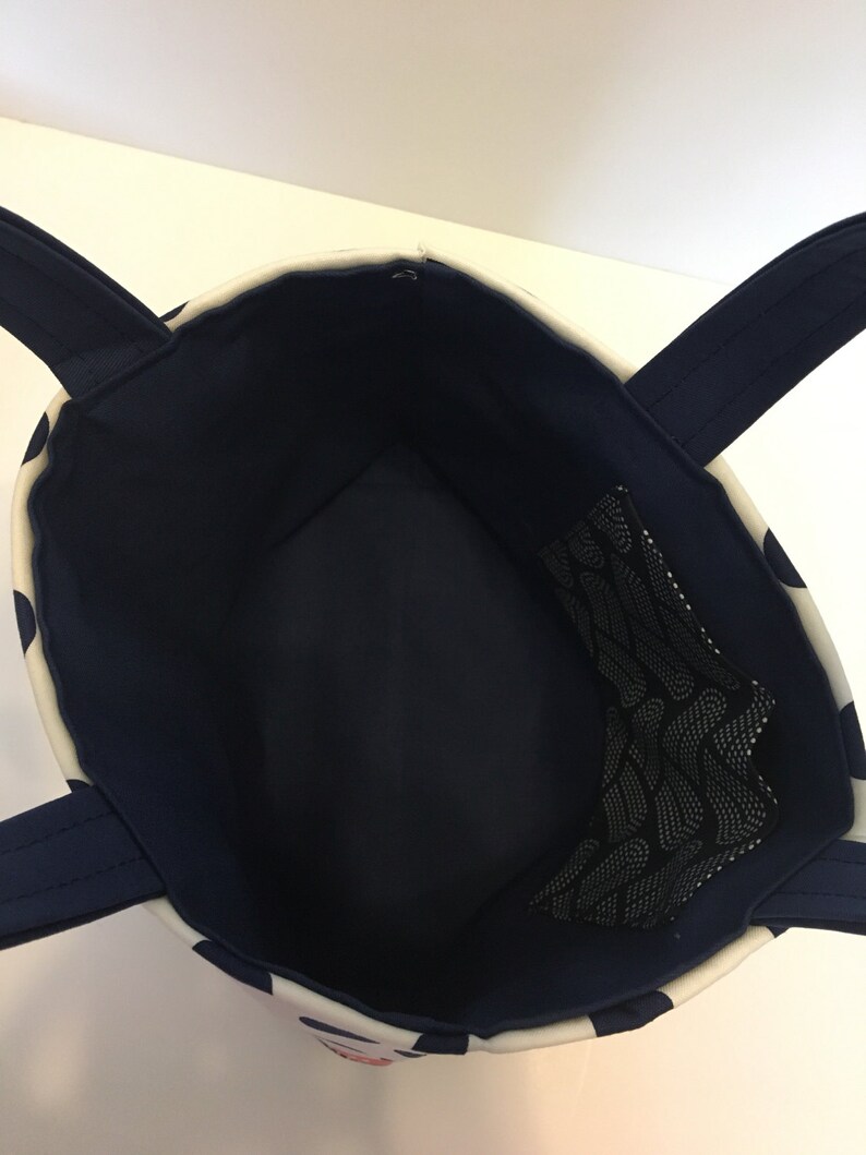 May include: A white and navy blue tote bag with a black mesh pocket inside. The bag has two navy blue handles.
