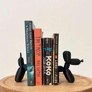 Puede incluir: Dos sujetalibros de perro globo en negro mate sostienen cuatro libros: The Last House on Needless Street, The Troop, Koko y Lord of the Flies. Los sujetalibros tienen forma de animales de globo estilizados con extremidades y hocicos redondeados.