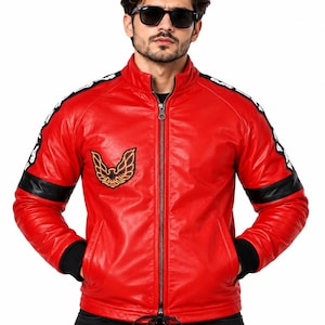 Puede incluir: Una chaqueta de color rojo brillante con cremallera frontal completa, cuello alzado y puños de canalé negros. Las mangas presentan franjas negras con texto blanco, y el pecho muestra un emblema de águila bordado en negro, naranja y amarillo.