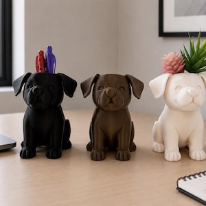 May include: Three dog-shaped containers in black, brown, and white. The black container holds a red and a blue pen. The white container holds a small pink succulent and a green spiky plant. Each container features a puppy design with floppy ears.