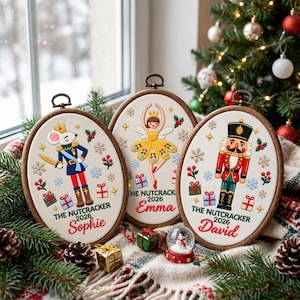 May include: Three oval wooden embroidery hoops featuring Nutcracker-themed designs on white fabric. The left hoop shows a mouse in a uniform, the centre a fairy, and the right a soldier. Each includes the text THE NUTCRACKER 2026 and a name.