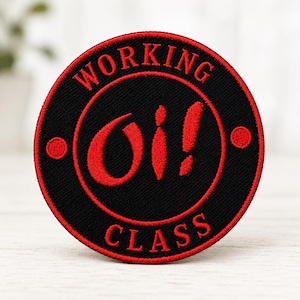 May include: A circular embroidered patch featuring a black background with a red border. The text "WORKING" is arched at the top and "CLASS" at the bottom in red. The center displays the red text "Oi!" with a red dot on each side.