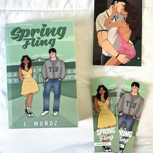 Pode incluir: Um livro intitulado Spring Fling de J. Muñoz, uma impressão artística de um casal a beijar-se e dois marcadores com as mesmas personagens. A capa do livro e os marcadores mostram uma pessoa com um vestido amarelo e uma com um casaco TLU cinzento.