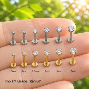 May include: Two rows of six labret studs with clear round gemstones. The top row is silver-toned, and the bottom row is gold-toned. Sizes range from 1.5mm to 5mm, as labeled. The text Implant Grade Titanium is printed at the bottom.