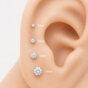 Può includere: Quattro orecchini a lobo rotondi, trasparenti e sfaccettati, disposti verticalmente su un modello di orecchio. Gli orecchini sono etichettati con le rispettive dimensioni: 3mm, 4mm, 5mm e 6mm. Ogni orecchino presenta una montatura in metallo.
