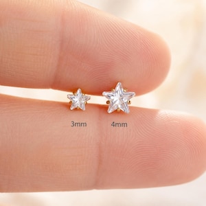 May include: Two star-shaped stud earrings with clear, faceted stones set in gold-toned metal. The smaller star is labeled 3mm and the larger star is labeled 4mm, indicating their respective sizes in millimeters for clear identification.