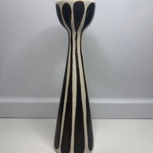 May include: A tall, tapered ceramic candle holder featuring a cream-colored base with vertical, dark brown, textured stripes that extend from the wide circular base up to the flared, bowl-shaped top designed to hold a single taper candle.