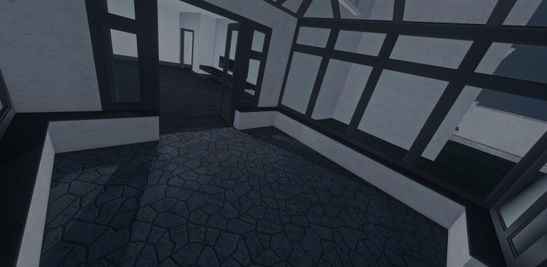 Op de afbeelding: Een binnenruimte met een donkere stenen vloer met een gebarsten patroon, witte muren en zwarte raamkozijnen. De kamer bevat een grote glazen wandstructuur en een open deuropening die leidt naar een tweede kamer met een donkere vloer.