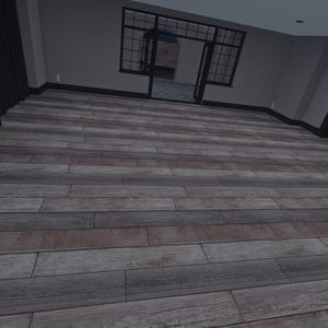 Op de afbeelding: Een binnenruimte met brede houten vloerplanken met een verweerd grijs en bruin houtnerfpatroon. De ruimte bevat een zwarte schoorsteenmantel, zwarte deurkozijnen en een zwarte boogvormige trapconstructie tegen lichtgrijze muren.