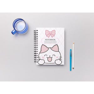 Può includere: Un quaderno a spirale con copertina bianca decorata da un fiocco rosa, la scritta NOTEBOOK e un gatto dei cartoni animati con orecchie rosa e lingua di fuori. Una penna blu, una matita bianca e una tazza di vetro blu sono accanto al quaderno.