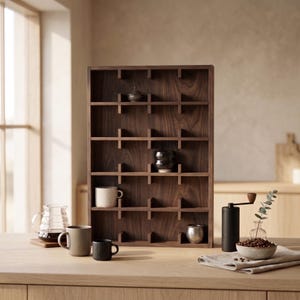 May include: A rectangular dark brown wooden display shelf with five horizontal tiers and vertical dividers creating multiple compartments. The shelf holds a small lidded jar, a dark ceramic bowl, and a metallic cup. Coffee accessories sit nearby.