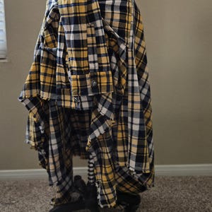 May include: A plaid flannel skirt in yellow, navy, and white, displayed on a dress form. The skirt has a high-low hemline and is made from a button-down shirt. The fabric has a classic lumberjack pattern.