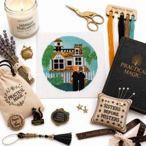 May include: A cross-stitch project of a house, a candle labeled Midnight Margaritas, a black book titled Practical Magic, a pin cushion with the text Sisters Before Misters, gold scissors, embroidery floss, a drawstring bag, and various small metal pins.